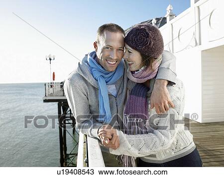 Stock Image - Couple holding hands, standing on pier, portrait. Fotosearch