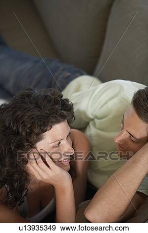 Couple looking at each other, lying on couch in living room, elevated view View Large Photo Image Stock Photo - Couple looking at each other, lying on couch in living room, elevated view. Fotosearch