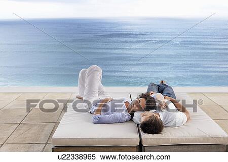 Couple lying down on sun beds on terrace overlooking sea, elevated view View Large Photo Image Stock Photography - Couple lying down on sun beds on terrace overlooking sea, elevated view. Fotosearch