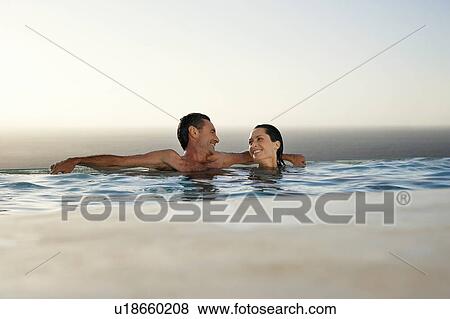 Stock Photo - Couple relaxing in infinity pool at sunset. Fotosearch