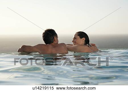Couple relaxing in infinity pool at sunset, back view View Large Photo Image Stock Photography - Couple relaxing in infinity pool at sunset, back view. Fotosearch