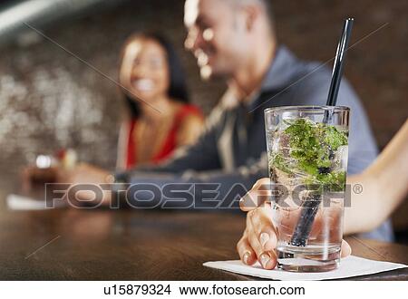 Couple sitting at bar, cocktail glass in foreground View Large Photo Image Picture - Couple sitting at bar, cocktail glass in foreground. Fotosearch