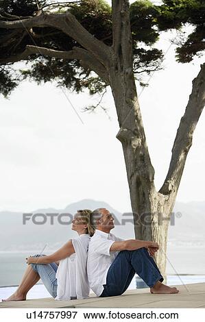 Couple sitting back to back on edge of infinity pool, side view View Large Photo Image Stock Photo - Couple sitting back to back on edge of infinity pool, side view. Fotosearch