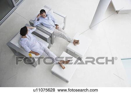 Stock Photo - Couple sitting in side by side armchairs, on terrace, elevated view. Fotosearch