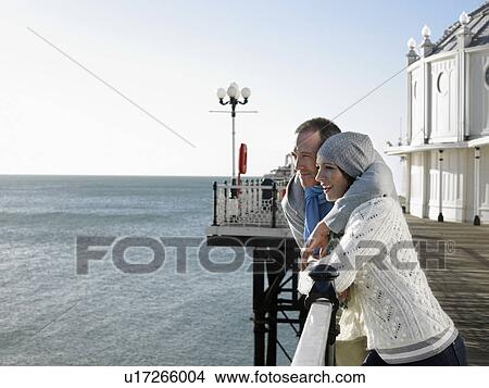 Picture - Couple standing on pier looking out at sea. Fotosearch