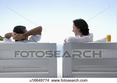 Picture - Couple talking, sitting on lounge chairs, outdoors. Fotosearch