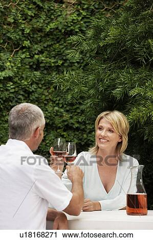 Stock Image - Couple toasting with wine glasses, sitting outdoors. Fotosearch
