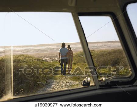 Stock Photo - Couple walking away from camper van towards beach, view through camper van window. Fotosearch
