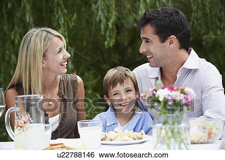 Stock Photograph - Couple with son (7-9) sitting at table in garden. Fotosearch