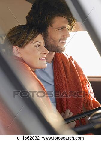Stock Image - Couple wrapped in blanket in front seat of van, profile. Fotosearch