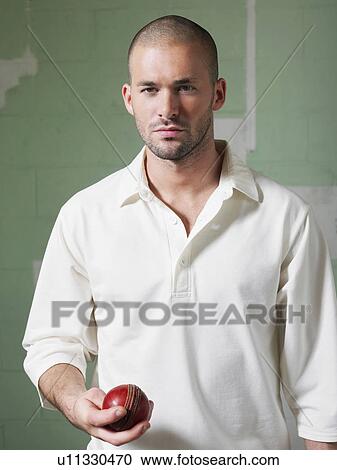 Stock Image - Cricket player holding ball, portrait. Fotosearch