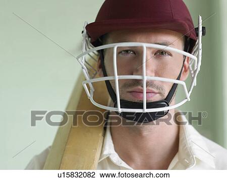 Stock Image - Cricket player wearing helmet and holding bat, close-up, portrait. Fotosearch