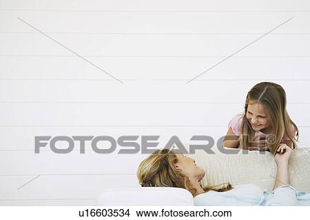 Picture - Daughter bending above mother lying on couch, half length. Fotosearch