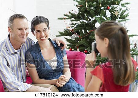 Picture - Daughter taking photo of mother and father by christmas tree. Fotosearch