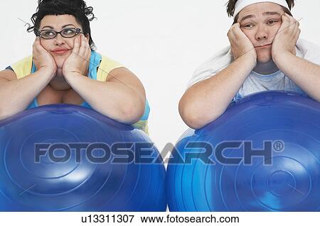 Stock Photo - Disinterested overweight man and woman lying on Exercise Balls, close up. Fotosearch