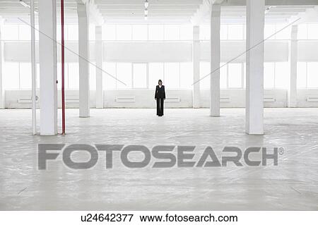 Stock Photo - Distant woman stands in empty warehouse. Fotosearch