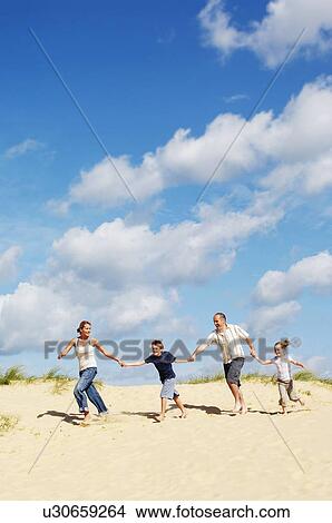 Picture - Family holding hands and running down sand dune on beach. Fotosearch