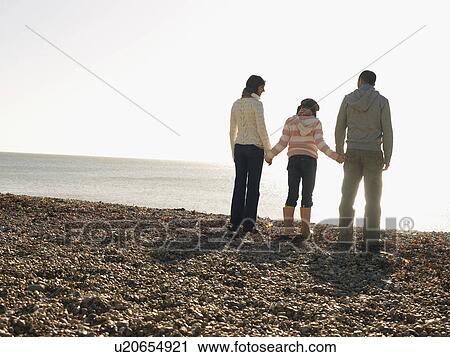 Family of three holding hands, standing on beach, back view View Large Photo Image Stock Image - Family of three holding hands, standing on beach, back view. Fotosearch