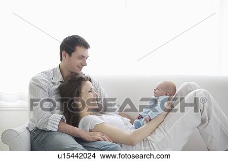Picture - Family of three on sofa with two week old newborn baby. Fotosearch