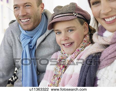 Stock Image - Family of three sitting side by side on bench, portrait, close up. Fotosearch
