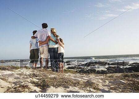 Stock Photo - Family standing together on beach, back view. Fotosearch