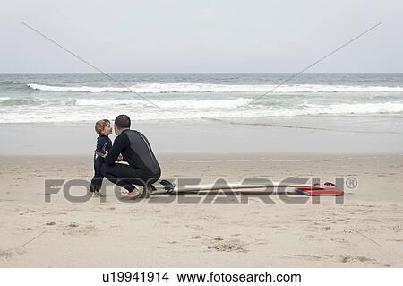 Father and son crouch in wet sand near surfboard View Large Photo Image Picture - Father and son crouch in wet sand near surfboard. Fotosearch