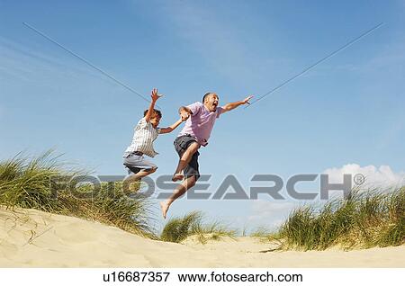 Father and Son holding hands jumping of sand dune at beach, low angle view View Large Photo Image Stock Photo - Father and Son holding hands jumping of sand dune at beach, low angle view. Fotosearch