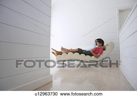 Stock Image - Father and son relaxing on lounge chair, full length. Fotosearch