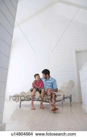 Picture - Father and son sitting on lounge chair, full length. Fotosearch