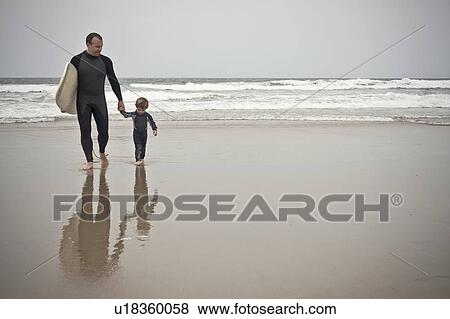 Stock Photo - Father and son walk back from sea carrying surfboard. Fotosearch