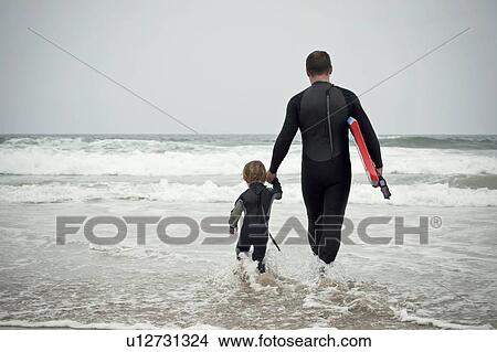 Father and son walk into the sea carrying bodyboard View Large Photo Image Picture - Father and son walk into the sea carrying bodyboard. Fotosearch