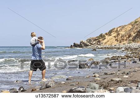 Father carries son on his shoulders at water's edge, CA View Large Photo Image Stock Photo - Father carries son on his shoulders at water's edge, CA. Fotosearch