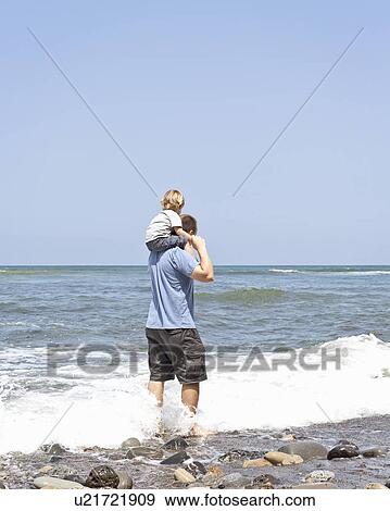 Stock Photo - Father carries son on his shoulders at water's edge, CA. Fotosearch