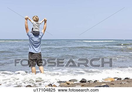 Stock Photography - Father carries son on his shoulders at water's edge, CA. Fotosearch