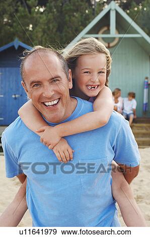 Stock Photo - Father giving daughter piggyback on beach, portrait. Fotosearch