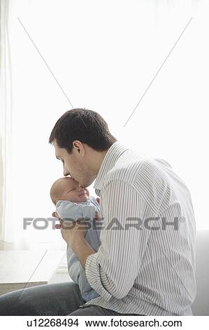 Picture - father kisses two week old newborn babies head. Fotosearch