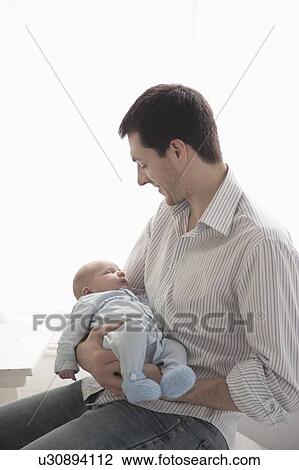 Stock Image - Father sits holding two week old newbord. Fotosearch