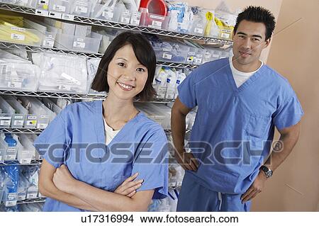 Picture - Female and male nurse standing by shelves with medical supply, portrait. Fotosearch