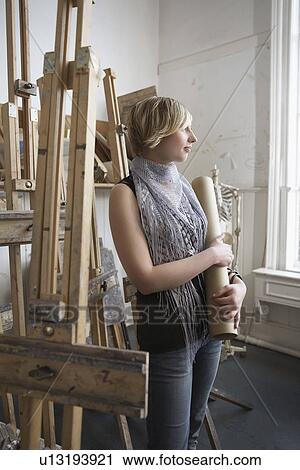 Stock Image - Female art student looking out of the window in studio. Fotosearch