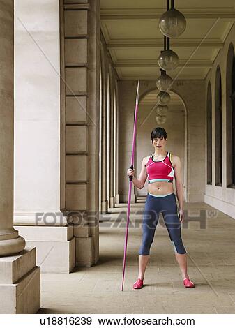 Stock Photo - Female athlete holding javelin, standing in portico, portrait. Fotosearch