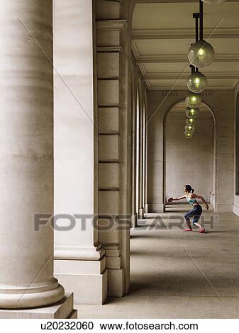 Stock Image - Female athlete throwing discus in portico, side view. Fotosearch
