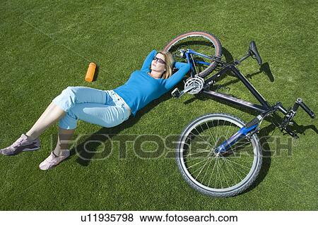 Female cylcist lying on grass with her bike View Large Photo Image Stock Photo - Female cylcist lying on grass with her bike. Fotosearch