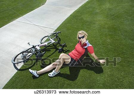 Stock Image - Female cylcist sits on grass beside path with her bike. Fotosearch