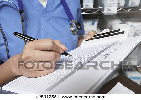 Stock Image - Female doctor writing in patient chart, mid section. Fotosearch