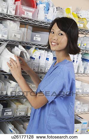 Stock Photo - Female nurse standing at shelf with medicines, portrait. Fotosearch