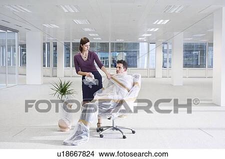 Female office worker unwrapping office worker in empty office space View Large Photo Image Picture - Female office worker unwrapping office worker in empty office space. Fotosearch