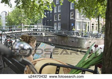 Stock Image - Female traveller looks at map on canalside in Amsterdam. Fotosearch