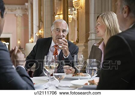Four business people sitting at restaurant table, talking View Large Photo Image Stock Photograph - Four business people sitting at restaurant table, talking. Fotosearch