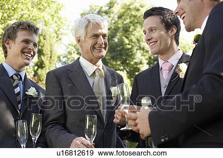 Stock Photo - Four men holding empty wineglasses, smiling. Fotosearch