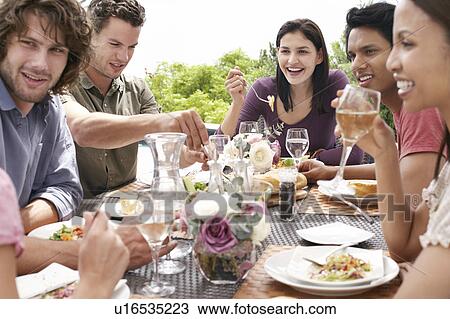 Stock Image - Friends eating drinking and socialising at table outdoors. Fotosearch